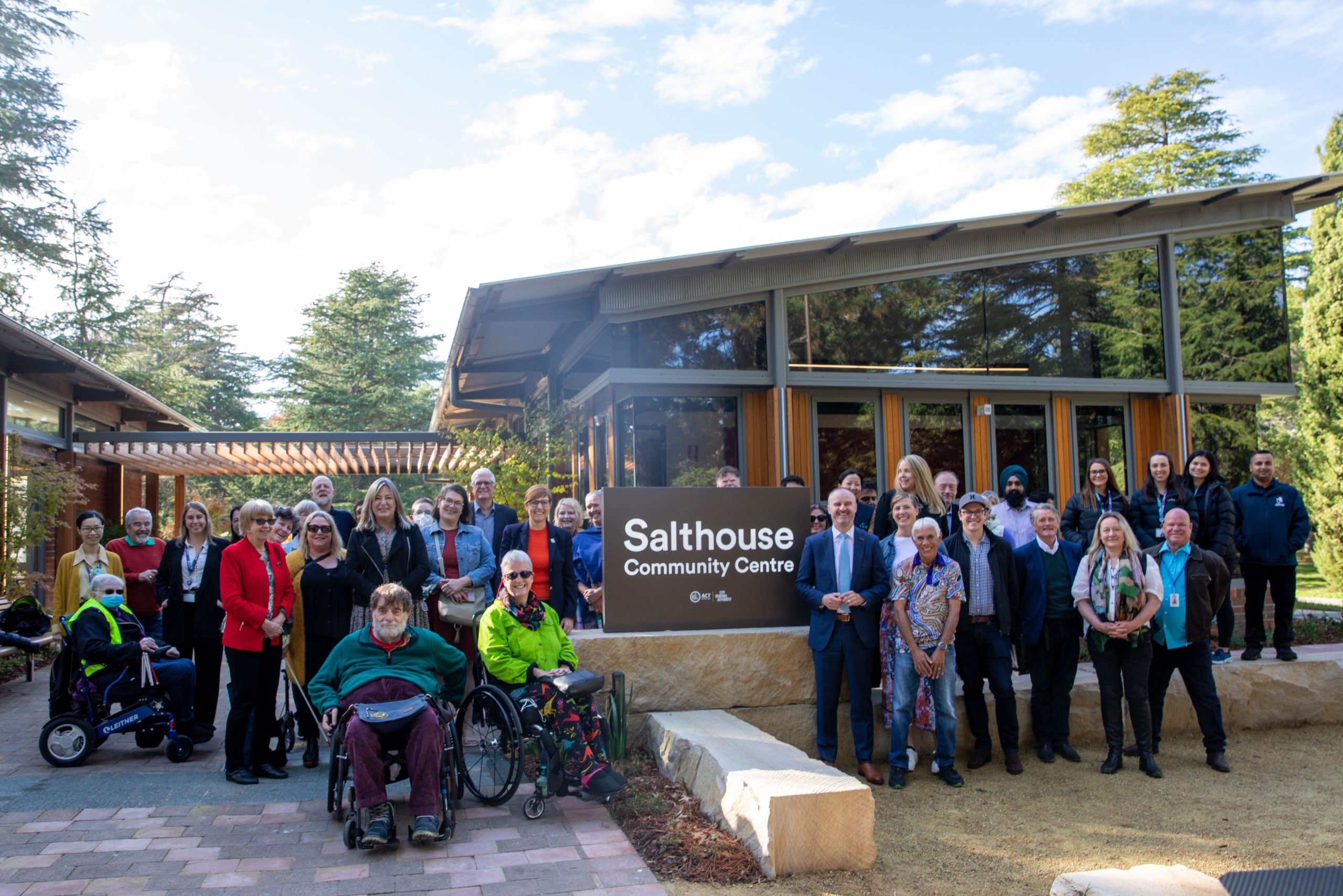 Image description: IMAGE: Attendees in a group pose, at the end of the naming ceremony for the new Salthouse Community Centre. All smiling at the camera. ACT Chief Minister Andrew Barr and Luisa Fearnside are standing to the right of the Community Centre's sign. Image source: ACT Government
